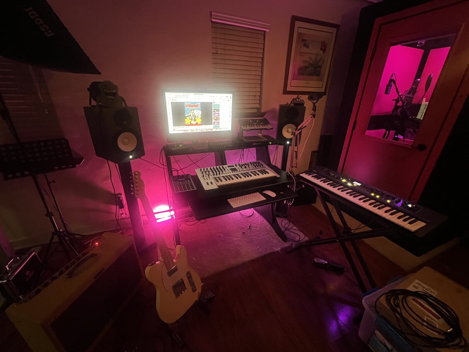 Production setup with synthesizers, keyboards, monitors, and vocal booth
